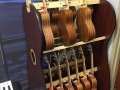 many wood ukuleles on shelves, in front of a window, next to a keyboard