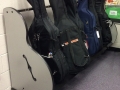 cello cases resting on a wheeled cart, in front of a cinderblock wall
