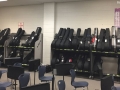the walls of a classroom lined with guitar racks, and blue chairs in the foreground