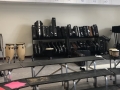classroom risers in the foreground with shelves of trumpet cases and bongos in the background