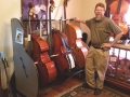 a bearded man standing next to a rack holding 3 double basses, placed on a carpet