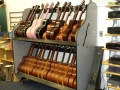 Many guitars resting on a shelf system to the right of a blackboard