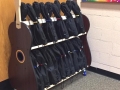 a wheeled cart, filled with black ukulele cases, next to a cinderblock wall